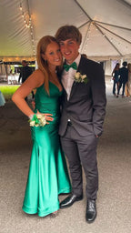 Young couple at prom in formal attire, woman in green satin dress, man in black suit with green bow tie, under event tent