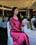 Woman in magenta satin dress seated at elegant event with string lights, ZAPDRESS fashion