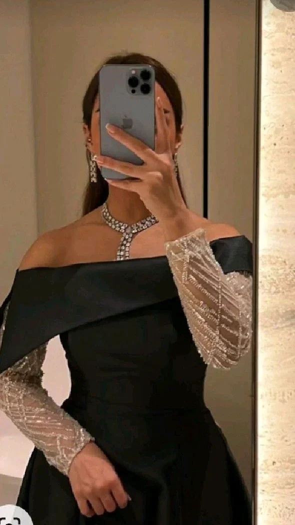 Woman in elegant black off-shoulder dress with sheer sleeves and statement jewelry, ZAPDRESS fashion