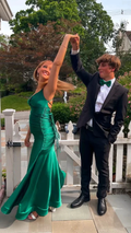 Young couple dressed for prom; woman in elegant green satin dress, man in black suit outside.