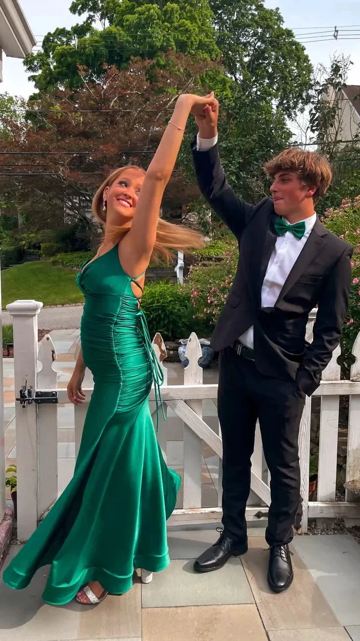 Young couple dressed for prom; woman in elegant green satin dress, man in black suit outside.