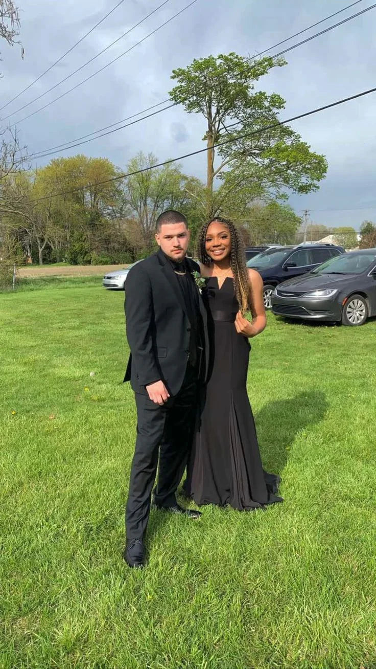 Couple in formal black attire posing on grass with cars and trees, ZAPDRESS style