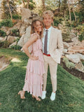 Young couple in formal attire, pink ruffle dress and tan suit, posing outdoors in garden