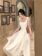 Elegant woman in flowing white dress holding a purse, walking indoors past framed pictures, ZAPDRESS fashion
