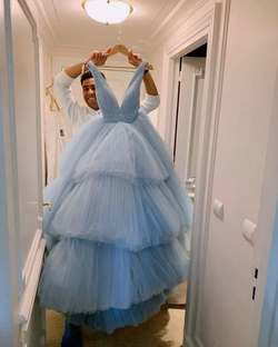 Man holding tiered blue tulle dress in bright hallway for ZAPDRESS fashion collection