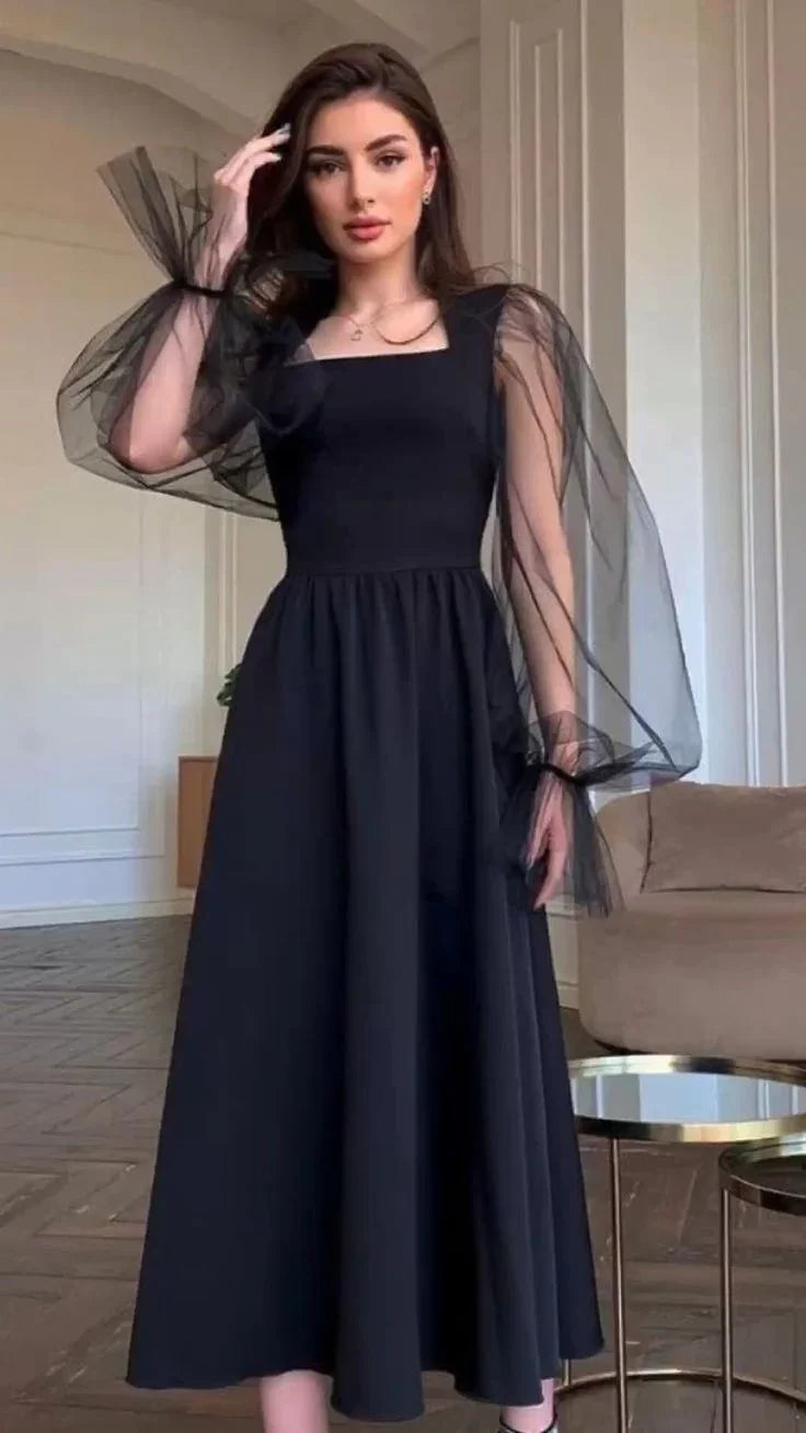 Woman wearing elegant black midi dress with sheer puff sleeves in modern living room, ZAPDRESS fashion