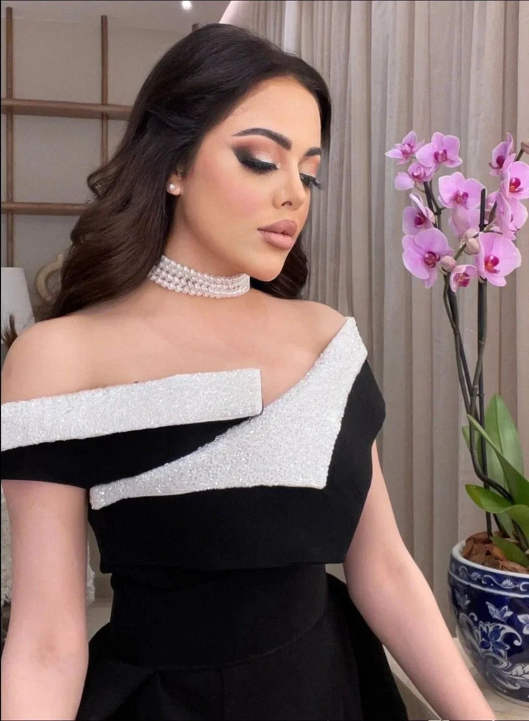Woman in elegant black and white off-shoulder dress from ZAPDRESS, pearl choker, orchid decor