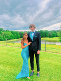 Couple in formal attire on lawn, woman in turquoise dress, man in black suit with turquoise accents, outdoors near pond, ZAPDRESS style inspiration
