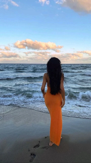 Woman in an orange dress stands on the beach facing the ocean at sunset, ZAPDRESS style