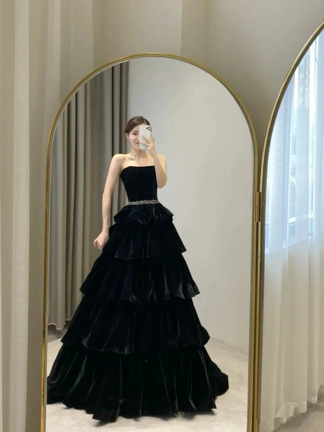 Woman modeling black tiered strapless evening gown in front of mirror, ZAPDRESS fashion