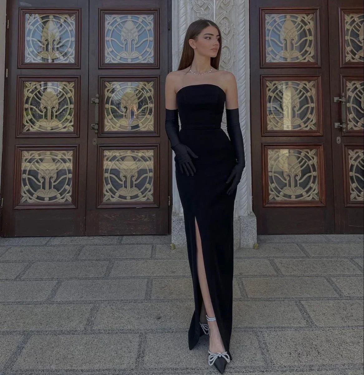 Elegant woman in black strapless evening gown with gloves, standing outside ornate doors, ZAPDRESS