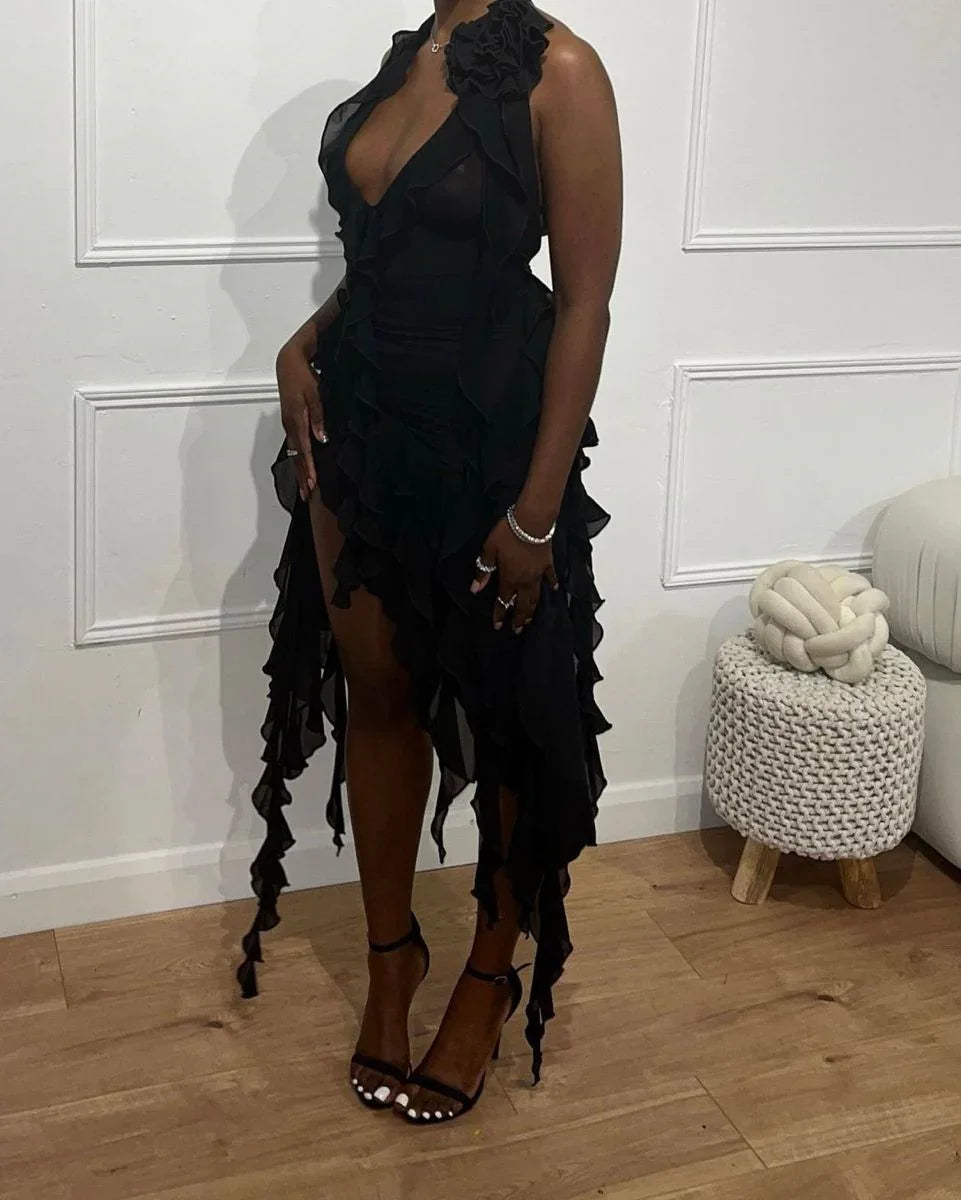 Woman wearing a black ruffled asymmetrical ZAPDRESS dress, standing indoors with minimal decor.
