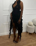 Woman wearing a black ruffled asymmetrical ZAPDRESS dress, standing indoors with minimal decor.