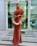 Elegant woman in a rust satin evening gown holding floral hoop bag, standing outside glass doors, ZAPDRESS fashion