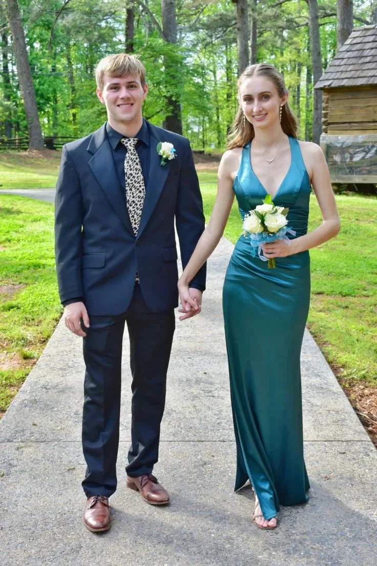 Young couple in formal wear, woman in teal dress, holding flowers, standing outdoors