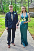 Young couple in formal wear, woman in teal dress, holding flowers, standing outdoors
