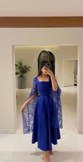 Woman in elegant royal blue dress with sheer sleeves in a modern, stylish room, ZAPDRESS fashion