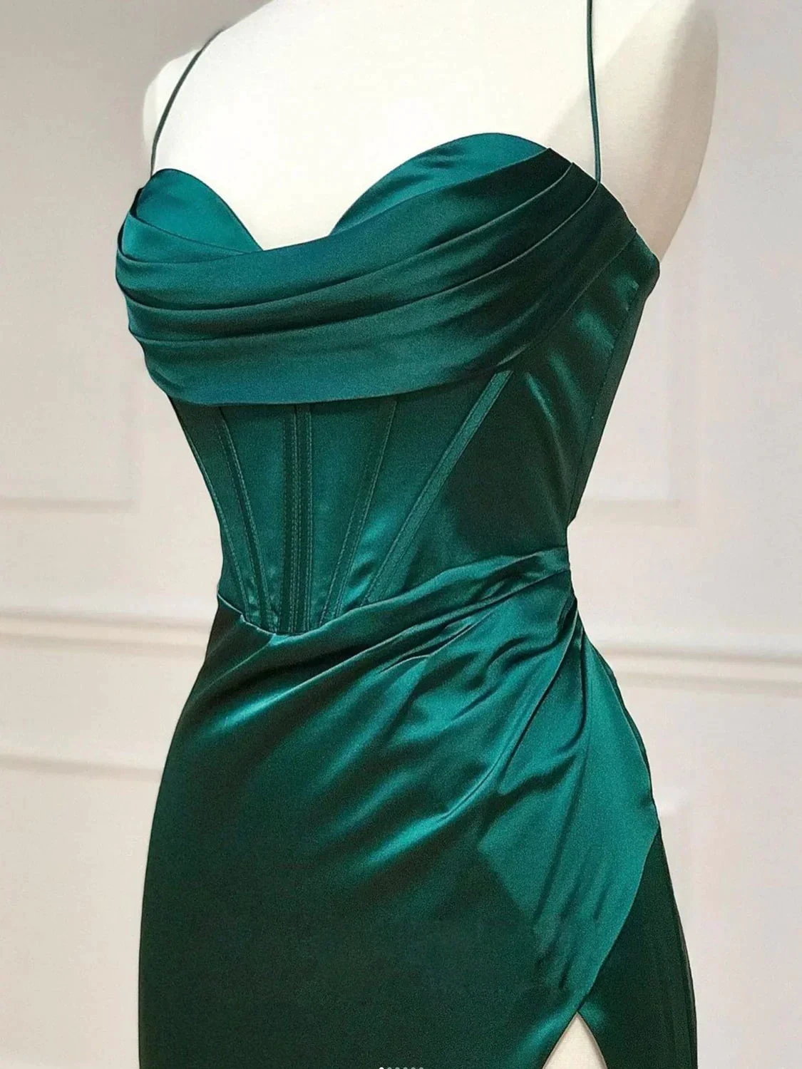 Emerald green satin evening dress with draped bodice and side slit, displayed on mannequin