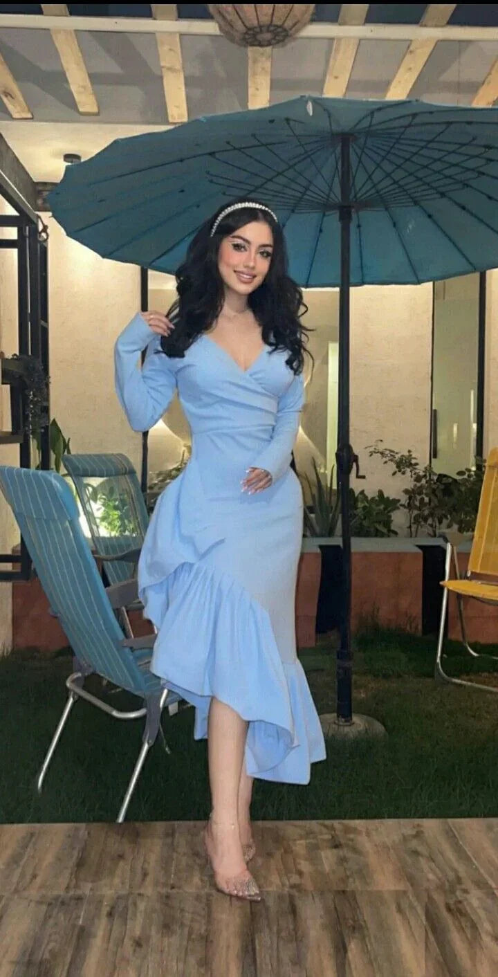 Woman in elegant light blue dress with ruffled hem posing outdoors at night under umbrella