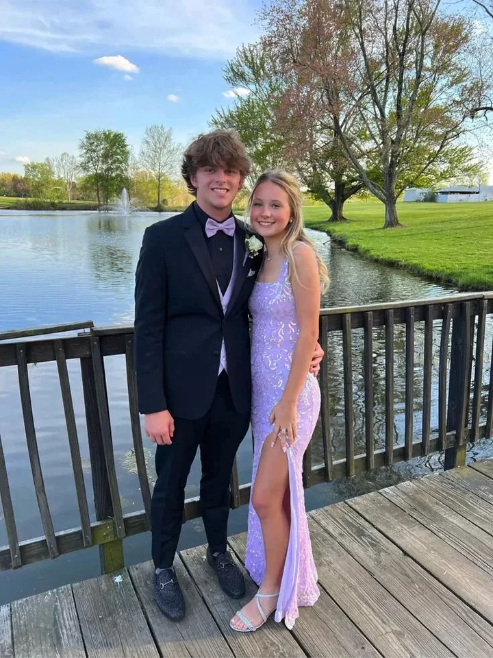 Young couple in formalwear, lavender prom dress and tuxedo, posing on wooden bridge by lake