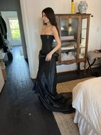 Woman wearing strapless black evening gown with train, standing in cozy bedroom, ZAPDRESS fashion