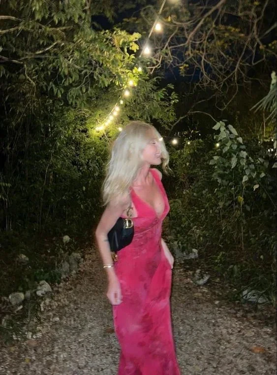 Woman in a vibrant red dress holding a black bag, walking on a forest path at night with string lights, ZAPDRESS