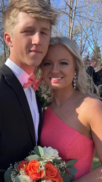 Young couple in formal attire with coral accents holding orange and white bouquet outdoors