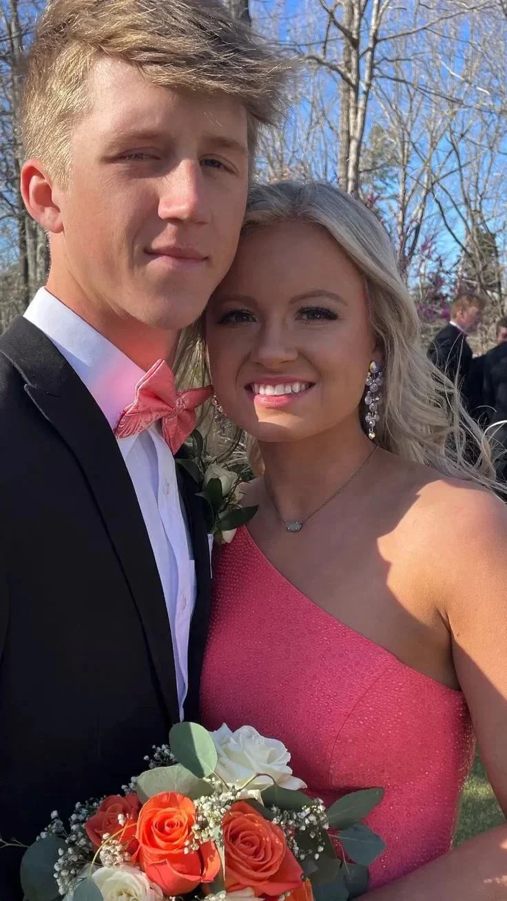 Young couple in formal attire with coral accents holding orange and white bouquet outdoors
