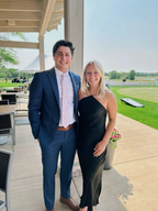 Man in blue suit and woman in black dress posing outside at event with green lawn background