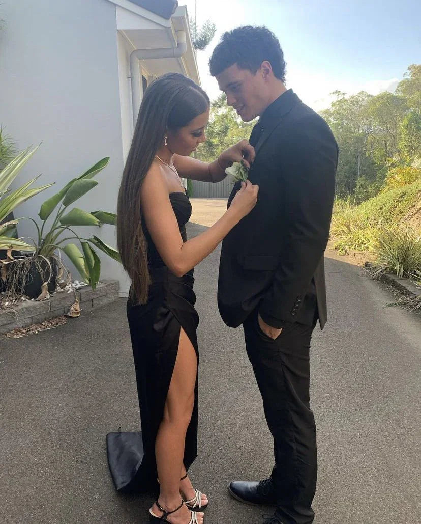 Young woman in a black prom dress pins boutonniere on man in suit outdoors, ZAPDRESS style