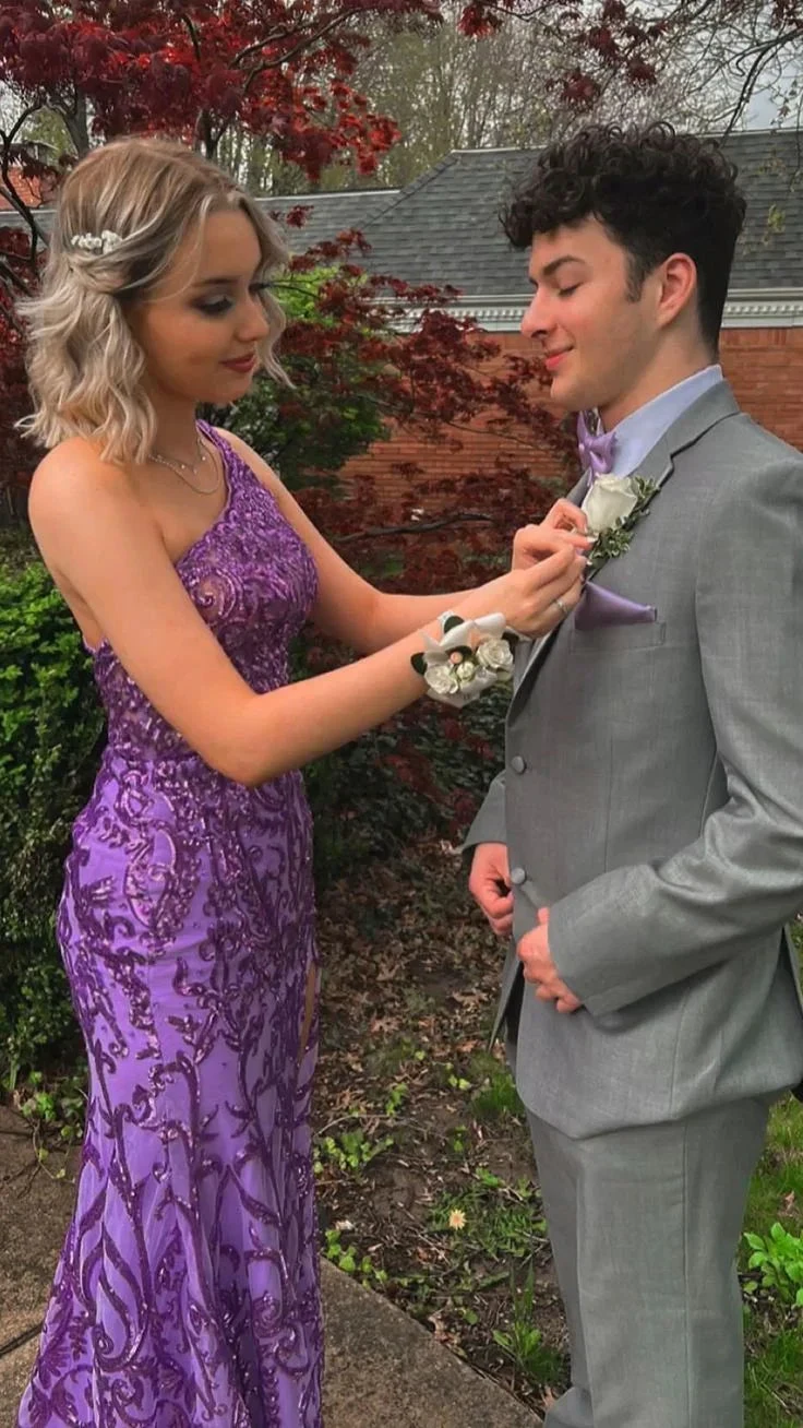 Young woman in a purple formal dress adjusting man's boutonniere outdoors at prom
