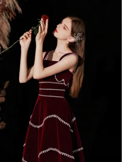 Woman in elegant burgundy ZAPDRESS dress holding a red rose against a dark background