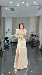 Woman in cream puff sleeve evening gown with high slit standing in modern living room, ZAPDRESS