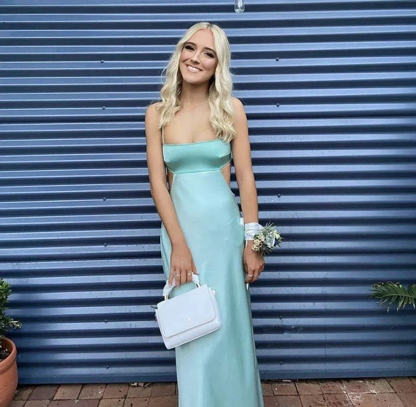 Woman in light blue satin formal dress holding white purse, posing by blue corrugated wall