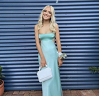 Woman in light blue satin prom dress holding white bag, standing in front of blue wall for ZAPDRESS