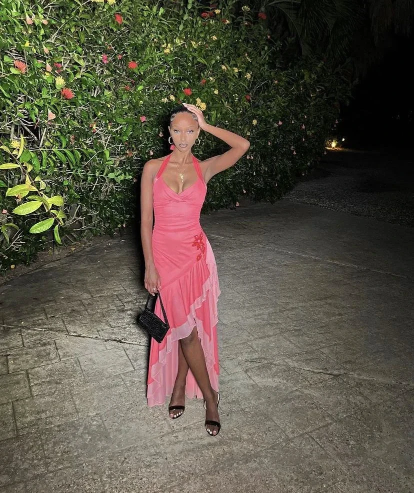 Woman in pink ruffled dress holding black purse, posing outdoors at night near greenery, ZAPDRESS