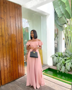 Woman in pink off-shoulder maxi dress holding black handbag, ZAPDRESS fashion, modern indoor setting