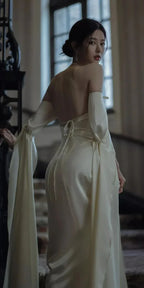 Elegant woman in backless ivory gown with long sleeves, posing on a staircase, ZAPDRESS