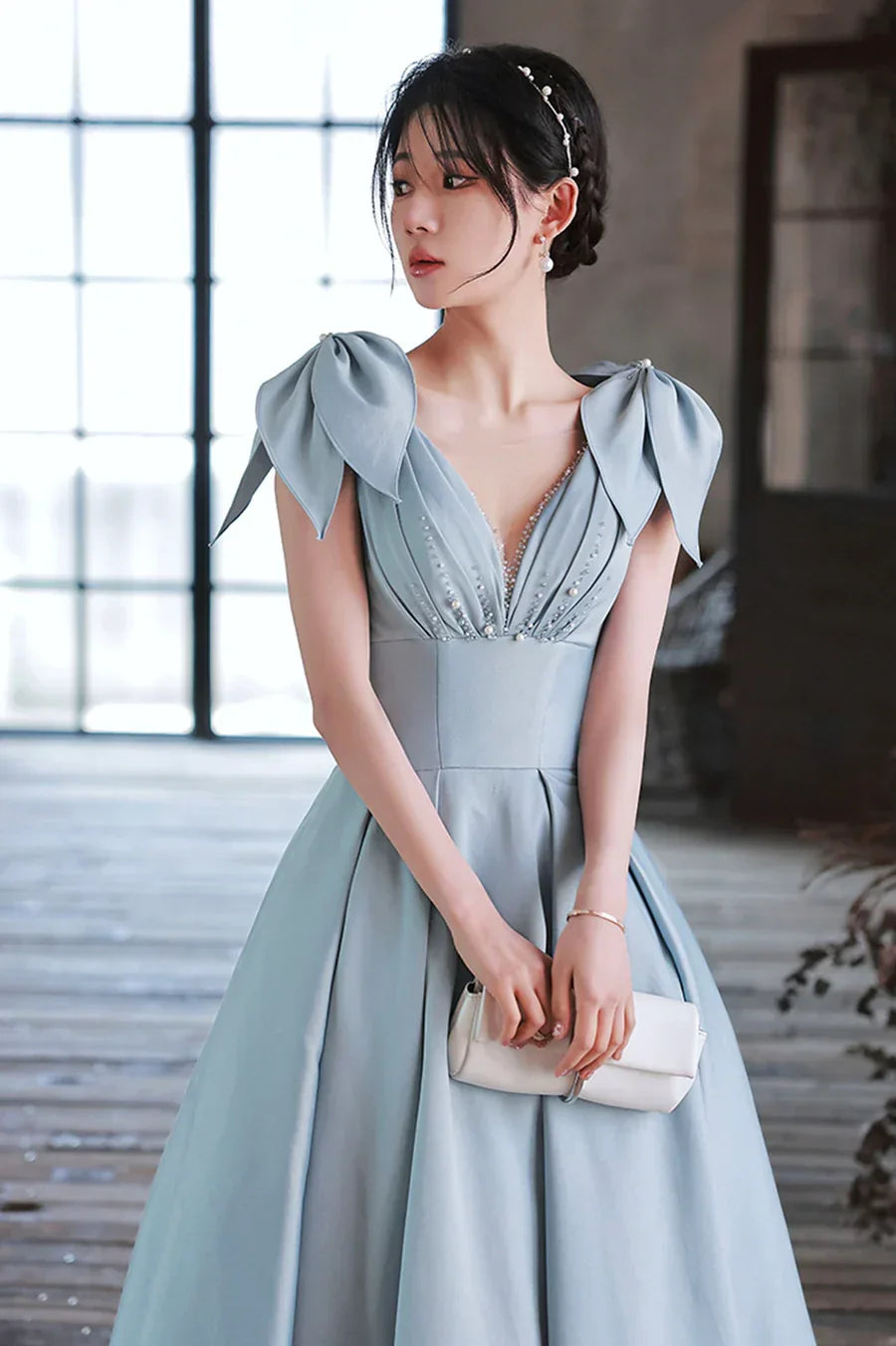 Elegant woman in powder blue evening gown with bow shoulders from ZAPDRESS, holding clutch