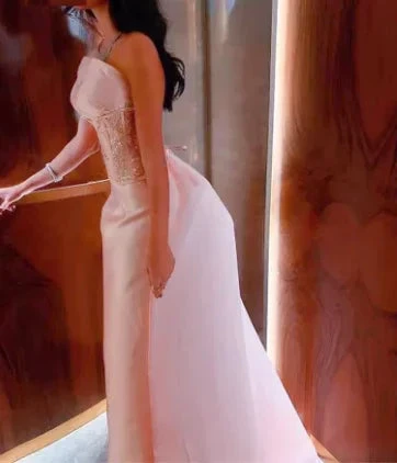 Elegant woman in a blush pink evening gown with lace bodice, standing by wood panel walls
