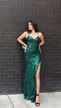 Woman in emerald green sequin evening gown with a side slit, posing by a black brick wall, ZAPDRESS