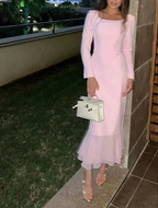 Woman in a long pink dress with ruffles, holding a white handbag, standing outdoors