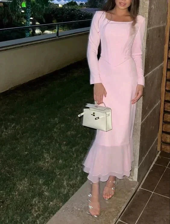 Woman in a long pink dress with ruffles, holding a white handbag, standing outdoors
