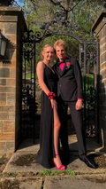 Young couple in formal black prom outfits and pink accents, posing by ornate wrought iron gate, ZAPDRESS style