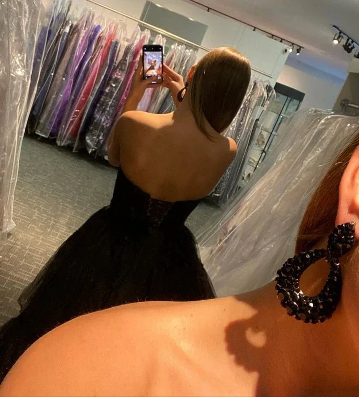 Woman in black strapless dress with statement earrings taking a mirror selfie at ZAPDRESS boutique