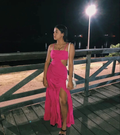 Woman in bright pink sleeveless dress with side cutout, standing on wooden boardwalk at night