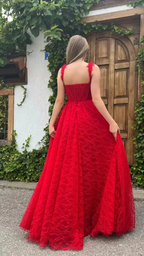 Woman in elegant red lace gown standing outdoors by a rustic wooden door, ZAPDRESS fashion