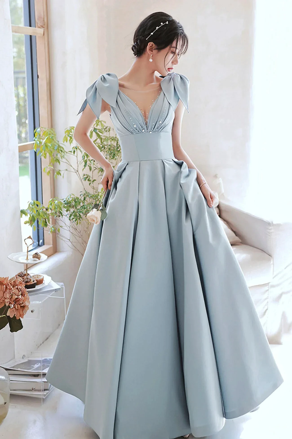 Elegant woman in a light blue evening gown with bow sleeves, showcased in a bright modern room.