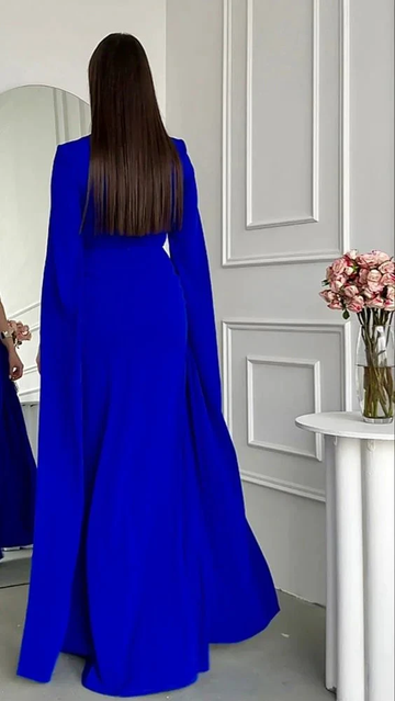 Woman in a royal blue evening gown by ZAPDRESS, standing in modern white room with flowers