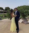 Elegant couple posing outdoors, woman in yellow maxi dress, man in navy suit, garden setting